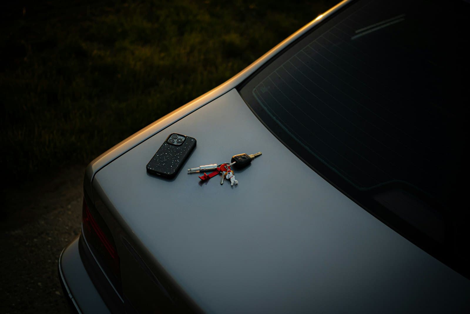 A phone and a bunch of car keys left on the boot lid of a grey coupé at dusk