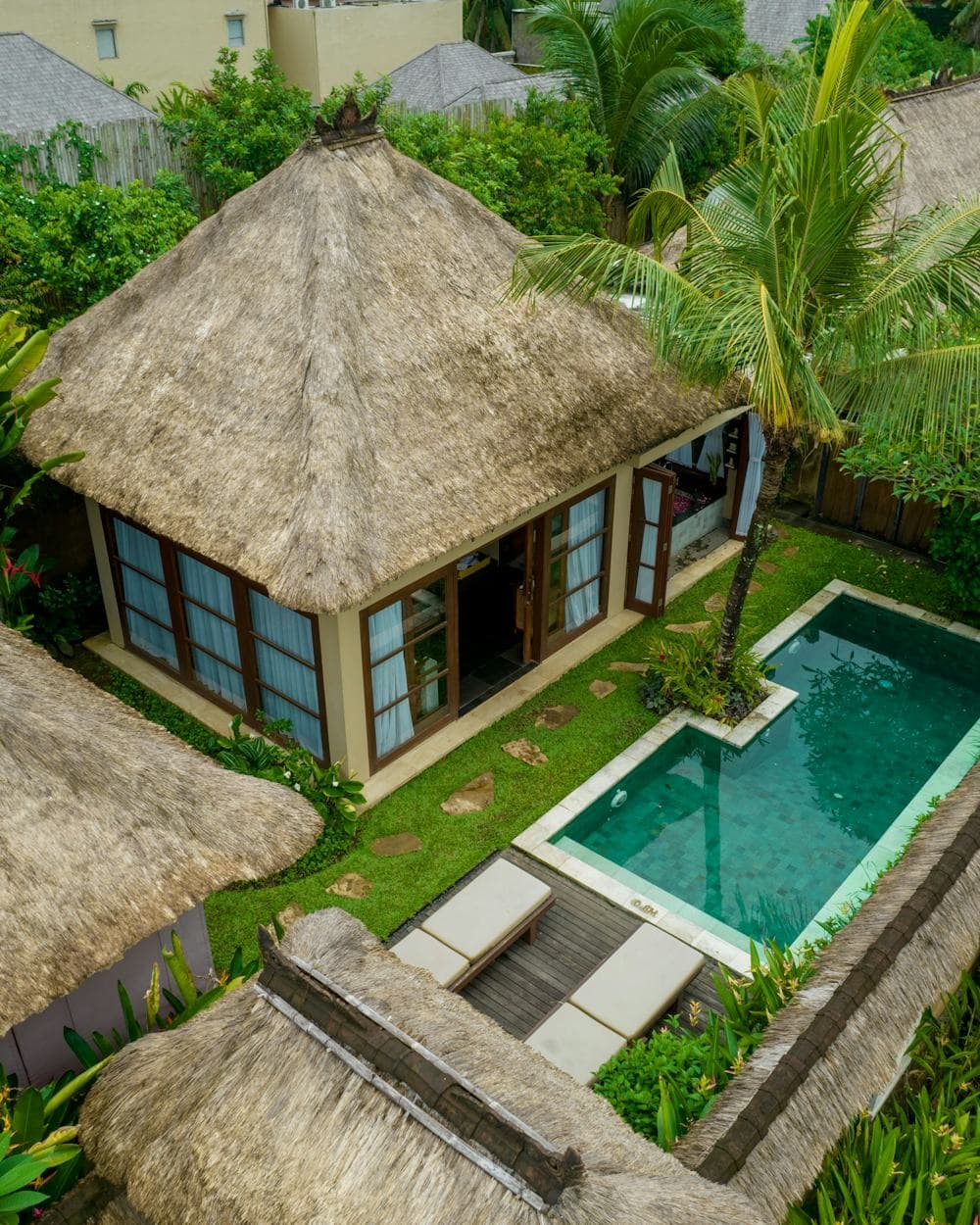 A thatched pavilion and its private pool seen from above, enclosed by dense tropical garden