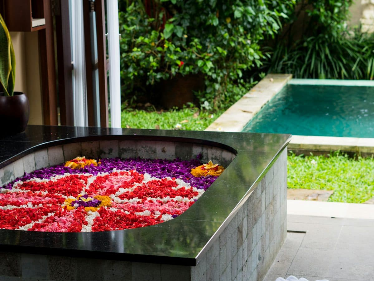 A stone bath filled with red, pink and purple flower petals beside a garden plunge pool