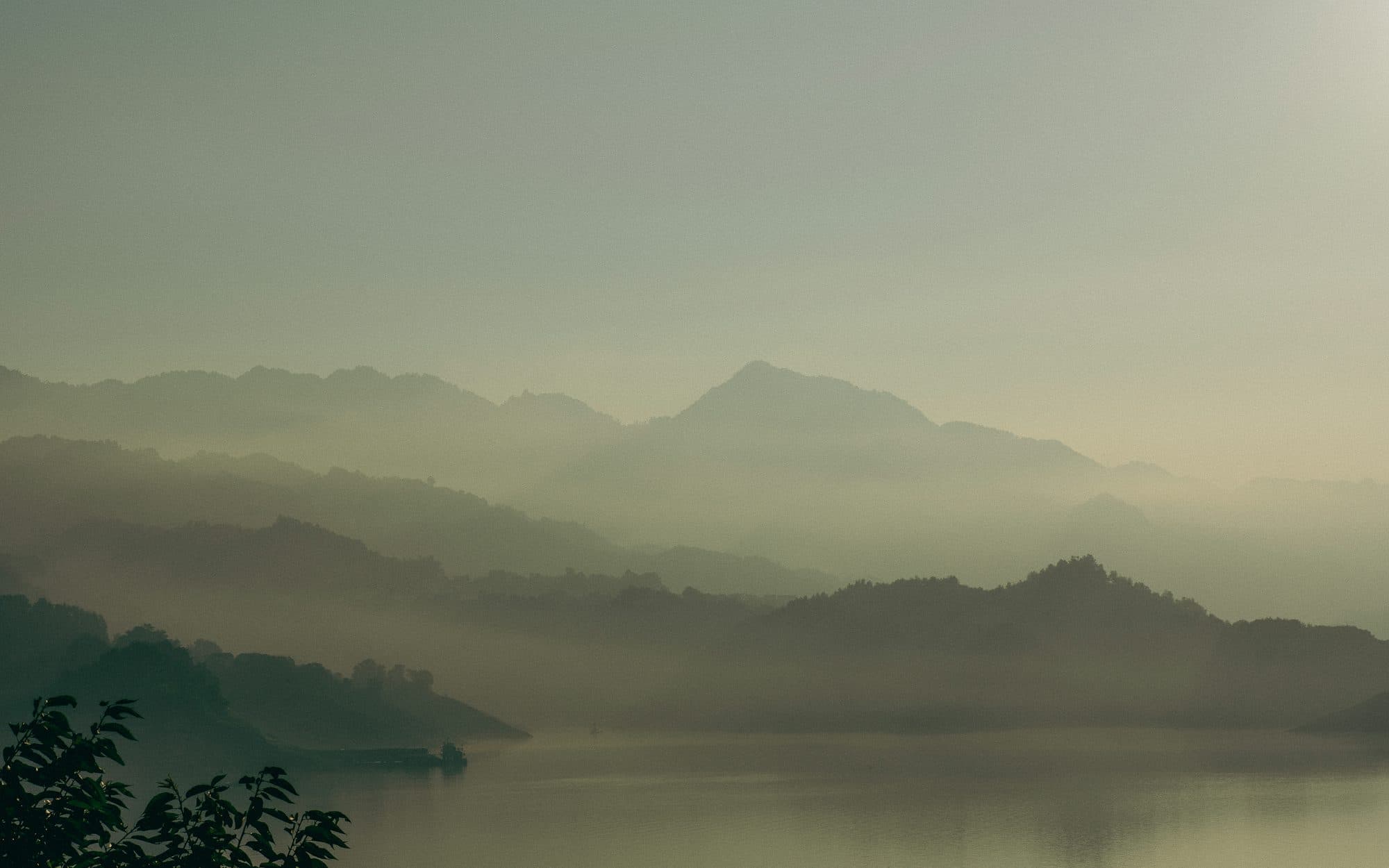 Layer upon layer of mountains dissolving into mist above a still lake at dawn