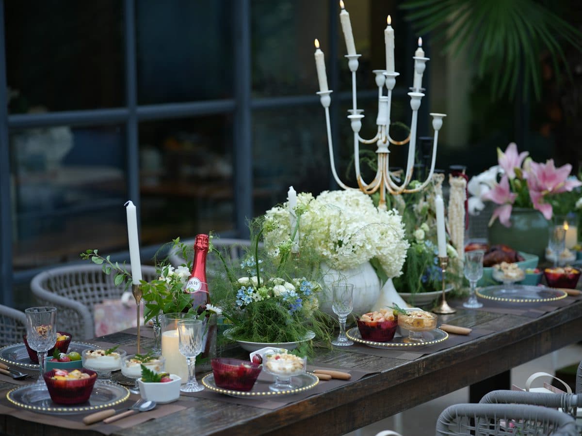 An outdoor table at dusk laid with candles, white flowers, glasses and small dishes