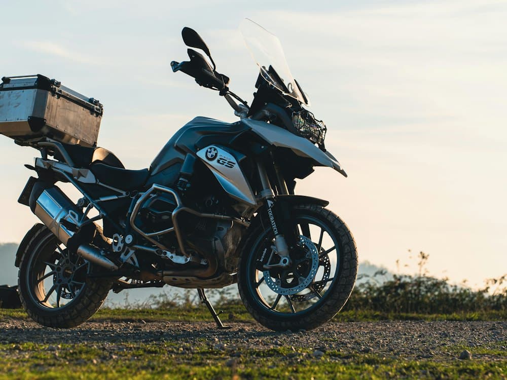A BMW R 1200 GS with an aluminium top box standing on gravel against a pale evening sky