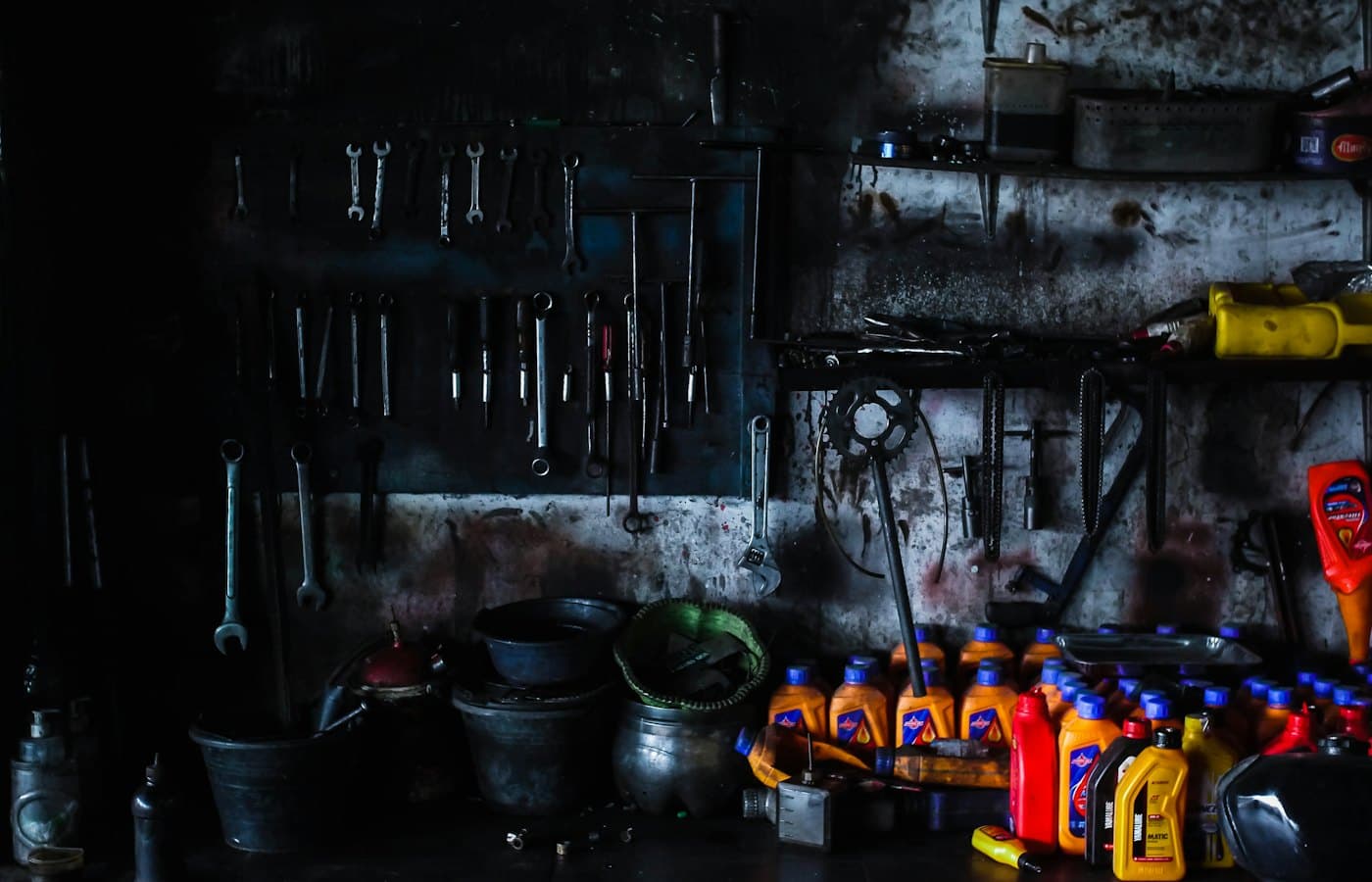 Spanners hanging in rows on a dark, oil-stained workshop wall above a bench crowded with oil bottles