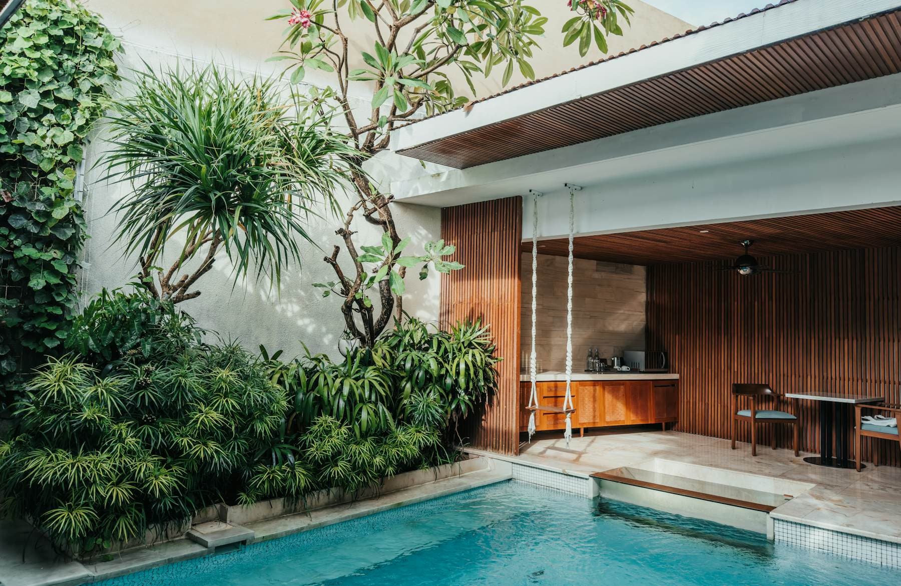 A courtyard pool with a teak-lined open sala, white walls and dense tropical planting