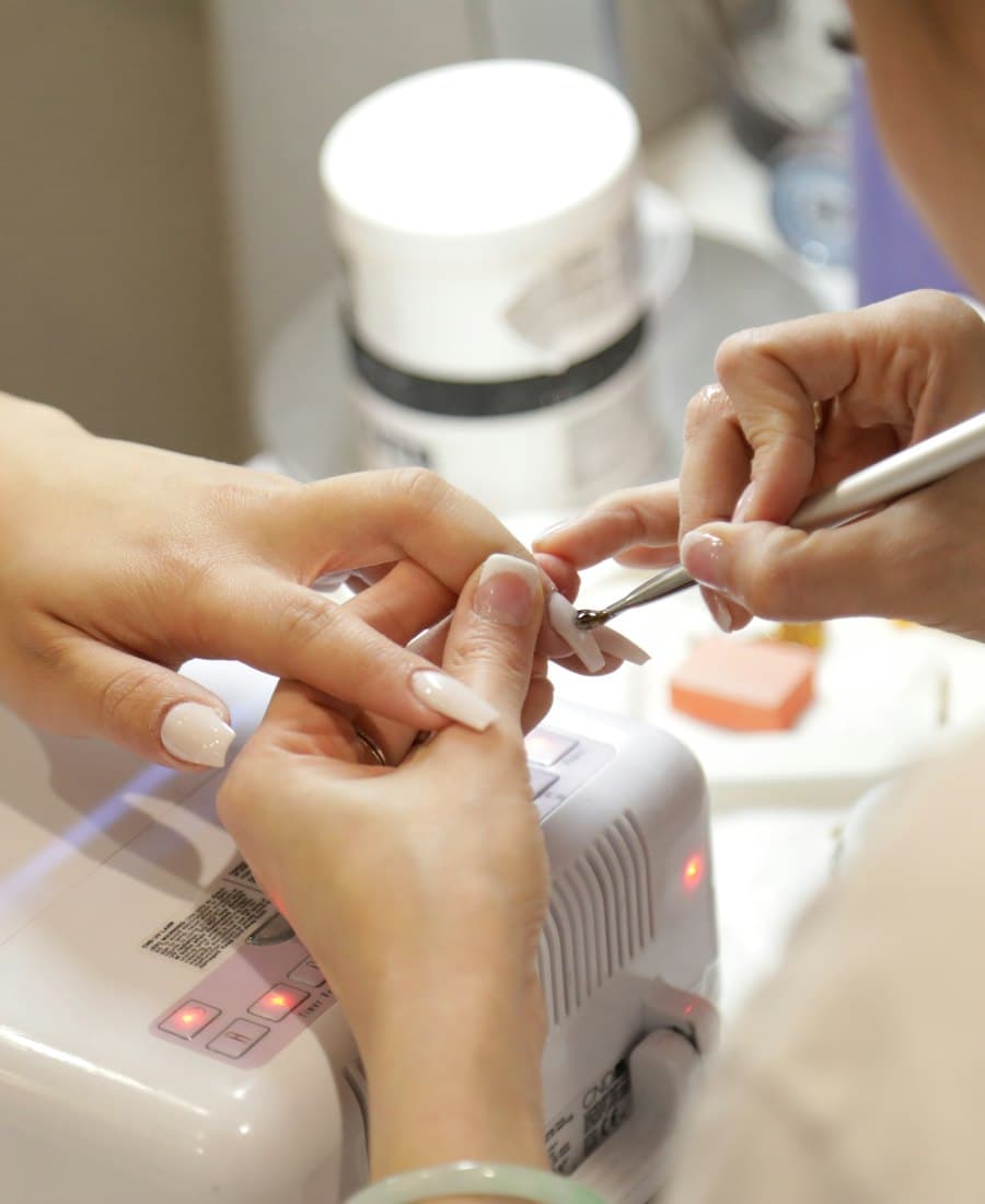 Close view of a nail artist’s hands filing a client’s nails over a white lamp