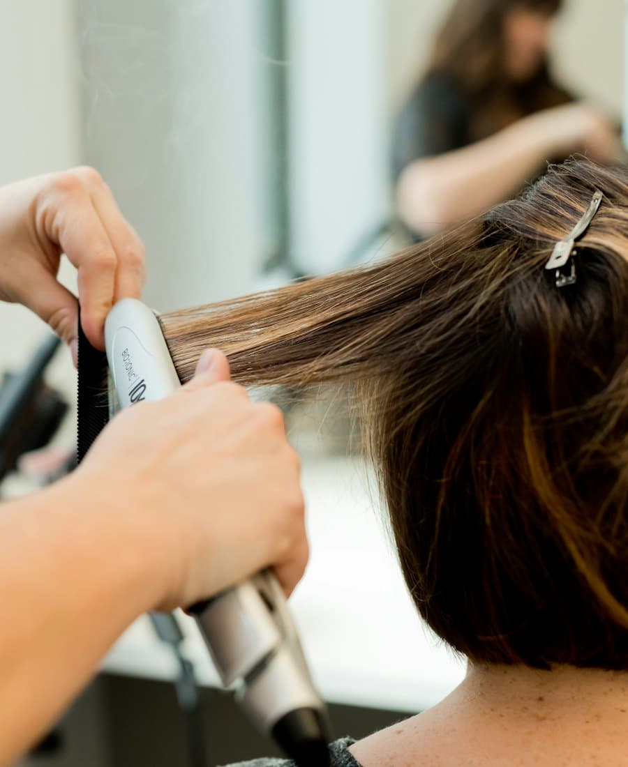 Hands running a curling iron through a section of clipped-up light brown hair