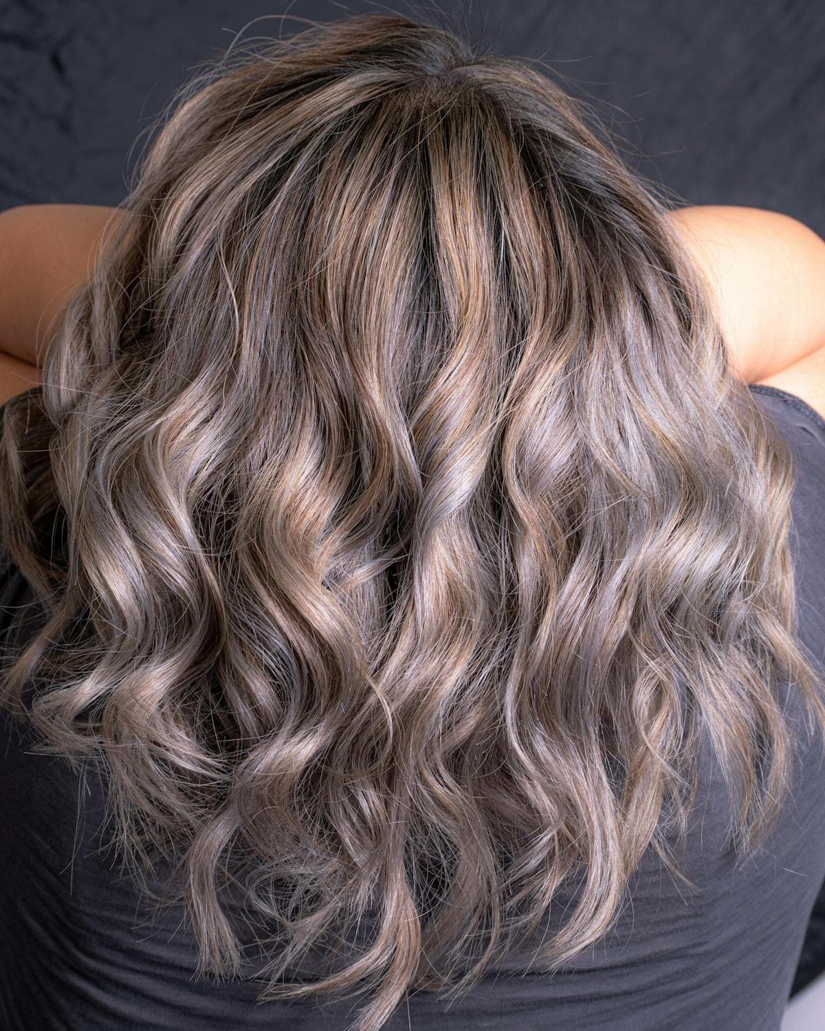 Thick mid-length hair in cool ash-brown curls, seen from behind