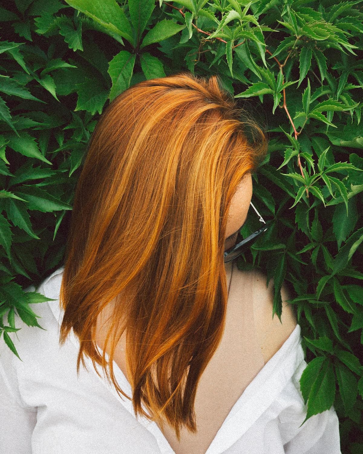 A bright copper-orange bob seen from behind against dark green leaves