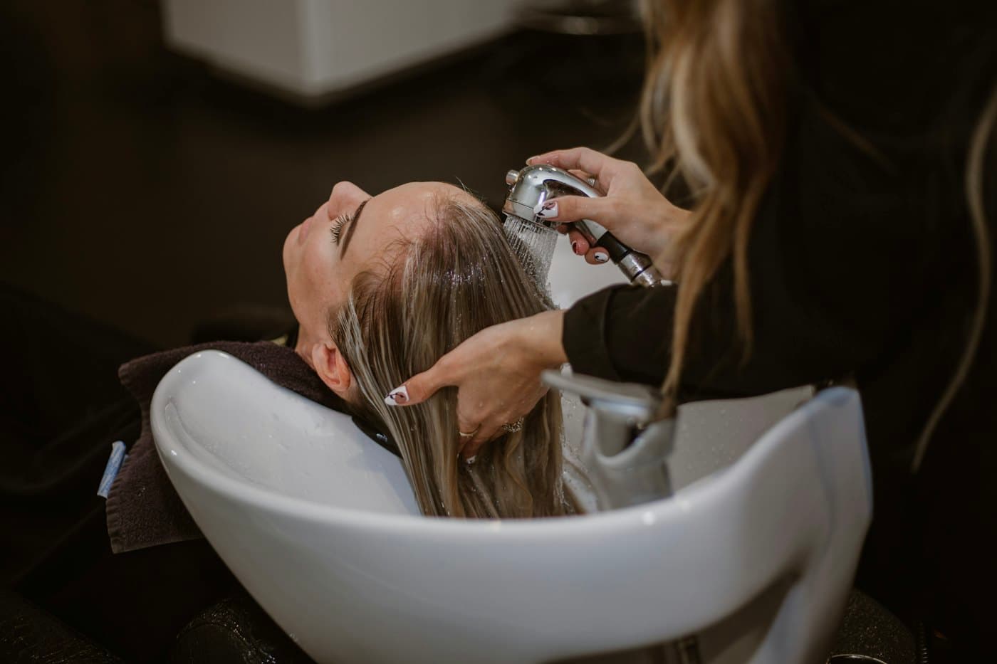 A guest lying back at a white basin while a stylist rinses her long hair
