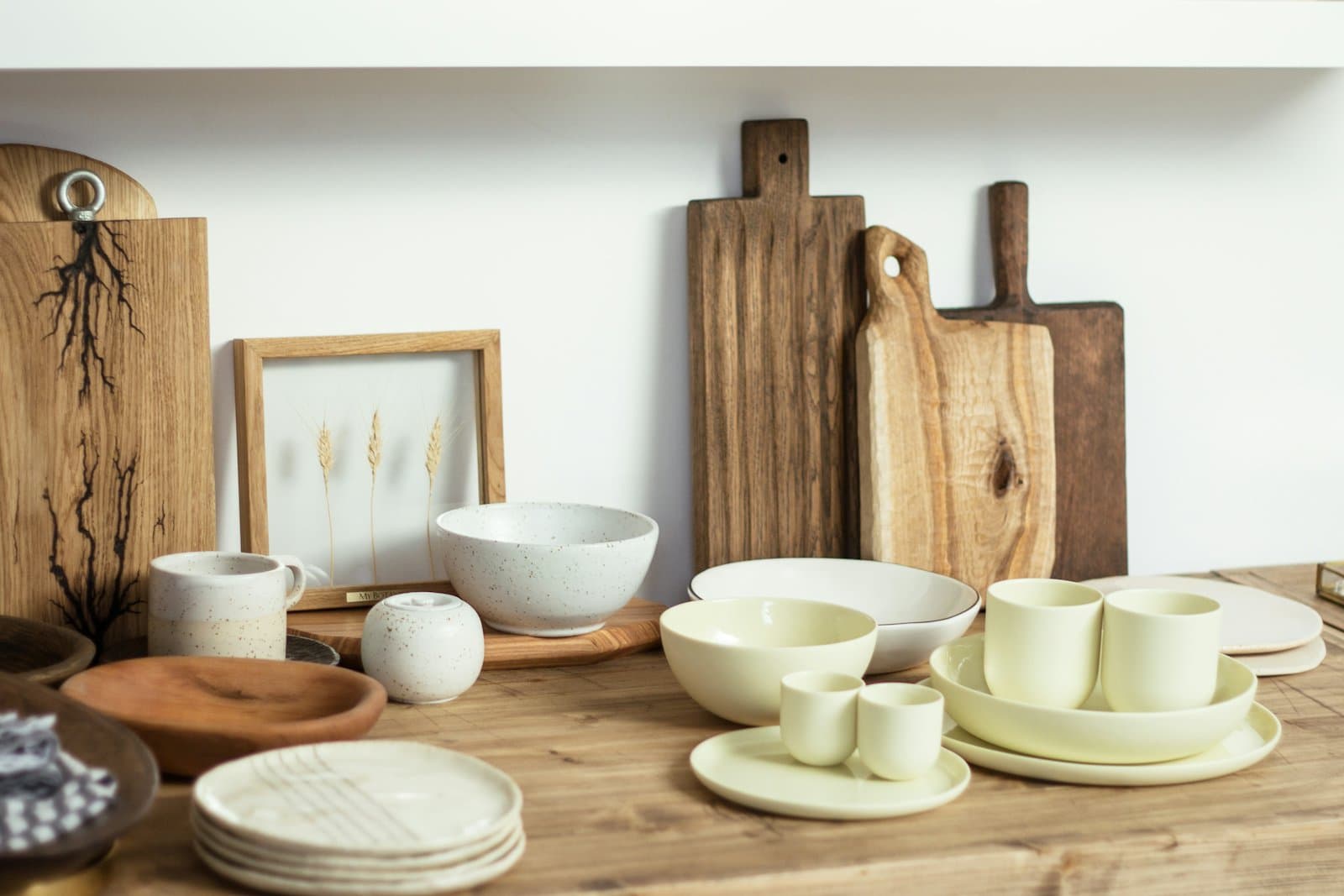 Bowls, cups and plates in white and pale glazes set out on a wooden table next to chopping boards